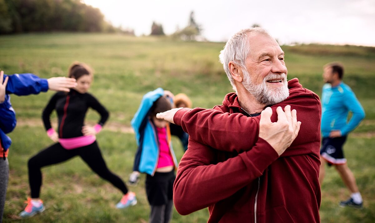 Older man stretching outside with exercise group lifestyle